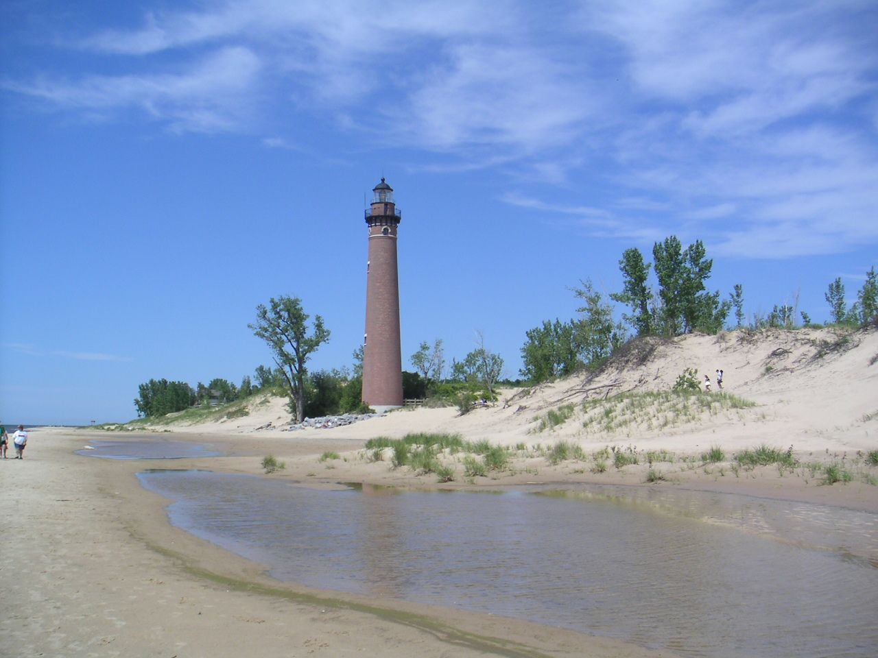 Little Sable Point Light, a tall red brick tower, seen across a shallow beach pool on a clear day.