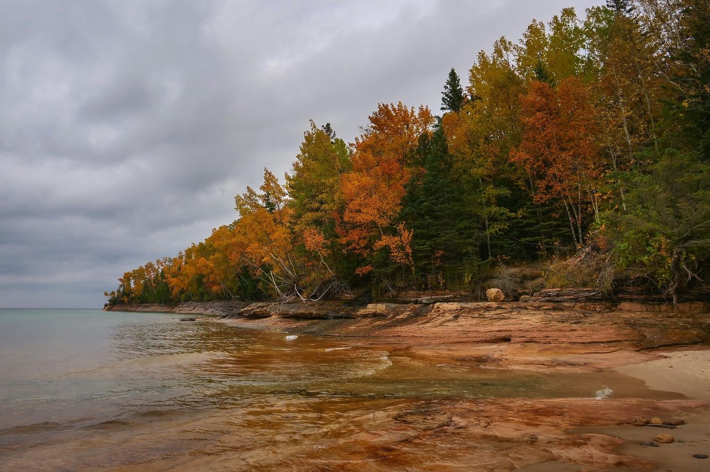 Golden and orange trees along a sandstone cliff above a beach at Pictured Rocks National Lakeshore.