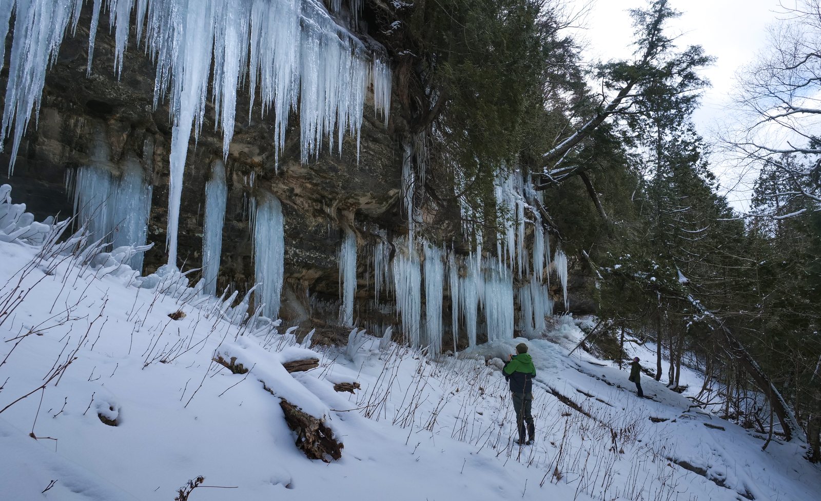 A person stands in front of tall blue ice curtains on the sandstone cliffs at Pictured Rocks National Lakeshore.